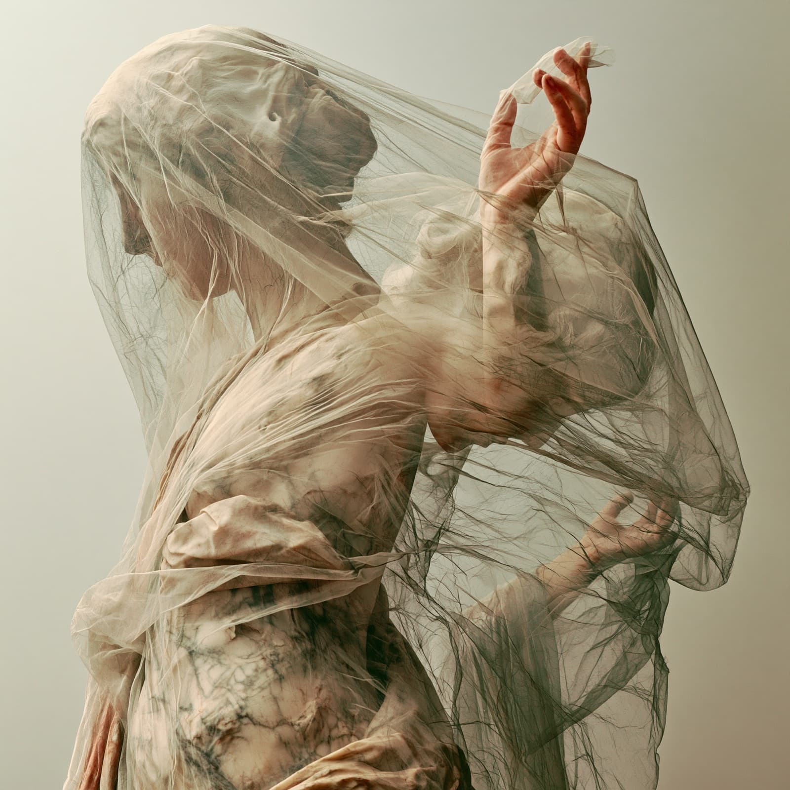 A marble figure draped in a translucent veil, one hand raised through the cloth.